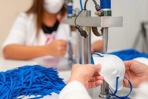 Women work at a machine for the manufacture of medical masks with nanofiber and solder loops to them with ultrasound. Coronovirus and Covid-19 Prevention photo