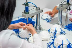 Women work at a machine for the manufacture of medical masks with nanofiber and solder loops to them with ultrasound. Coronovirus and Covid-19 Prevention photo