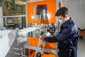 A man works at a machine for the manufacture of medical masks with nanofiber. Coronovirus and Covid-19 Prevention photo