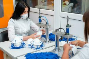 Women work at a machine for the manufacture of medical masks with nanofiber and solder loops to them with ultrasound. Coronovirus and Covid-19 Prevention photo