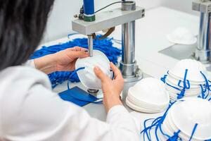 The girl works in a factory for the production of medical masks with nanofibre and solder loops with ultrasound on a machine. Coronavirus and Covid-19 Protection.Close-up. photo