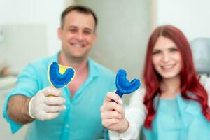 Happy doctor dentist with his patient show the result of impressions of her teeth on a spoon with silicone material photo