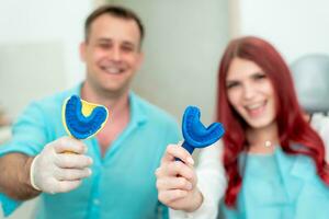 Happy doctor orthodontist with his patient demonstrate the result of impressions of her teeth on a spoon with silicone material photo