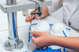 The girl works in a factory for the production of medical masks with nanofibre and solder loops with ultrasound on a machine. Coronavirus and Covid-19 Protection.Close-up. photo