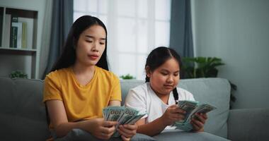 retrato de joven mujer y adolescente niña contando efectivo dinero en sofá en el vivo habitación a en casa, feliz contando dolares billete foto