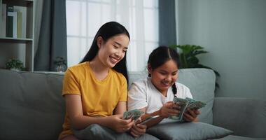 retrato de joven mujer y adolescente niña contando efectivo dinero en sofá en el vivo habitación a en casa, feliz contando dolares billete foto
