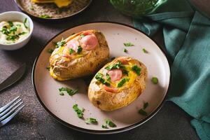 Baked potatoes in skins with egg and pieces of sausage on a plate on the table photo