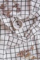 Change to winter time. Alarm clock and dried flowers on crumpled fabric top and vertical view photo