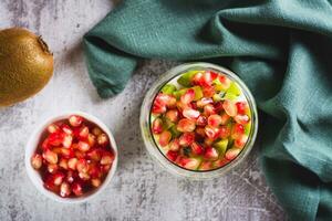 Close up of fresh greek yogurt with kiwi pieces and pomegranate seeds in a glass top view photo