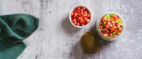 Tropical fruit kiwi, fresh yogurt and pomegranate seeds in a glass top view web banner photo