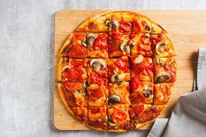 Close up of St. Louis Style pizza with bacon, mushrooms, tomatoes and peppers on a board top view photo