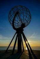 the sun sets behind a large globe in front of the ocean photo