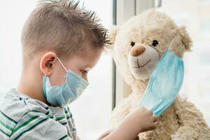 A small child helps a teddy bear put on a medical mask at home in quarantine. Prevention of coronavirus and Covid - 19. Concept photo