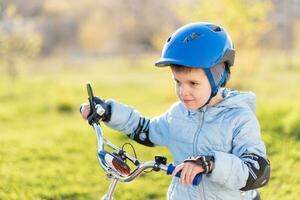 un niño en un casco aprende a paseo un bicicleta en un soleado día a puesta de sol foto