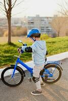 un niño en un casco aprende a paseo un bicicleta en un soleado día a puesta de sol foto