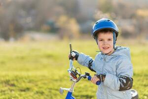 un niño en un casco aprende a paseo un bicicleta en un soleado día a puesta de sol foto