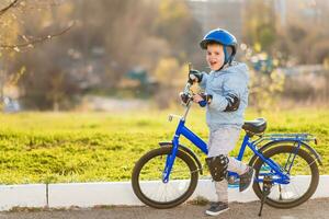 un niño en un casco aprende a paseo un bicicleta en un soleado día a puesta de sol foto