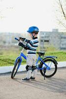 Cute child in helmet and protection stands near his bike photo