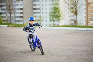 un niño en un casco y proteccion en un bicicleta paseo en naturaleza en el primavera foto