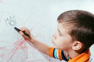 The child draws on the wall with a crayon. The boy is engaged in creativity at home photo