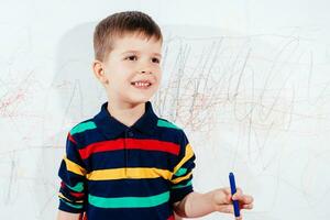 The child draws on the wall with a crayon. The boy is engaged in creativity at home photo