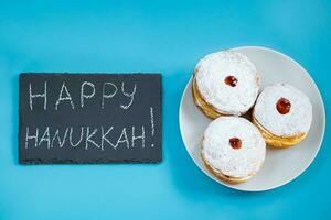 feliz Jánuca. postre judío sufganiyot donuts sobre fondo azul. símbolo de la fiesta del judaísmo religioso. inscripción en pizarra. foto