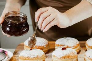 Woman chef prepares fresh donuts with jam at her bakery. Cooking traditional Hanukkah sufganiyot. Small business. photo