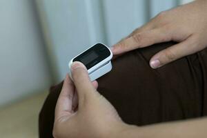 Woman resting at home using pulse oximeter to monitor blood oxygen levels and pulse rate. finger inserted into the pressure oximeter to assess health from the living room home. photo