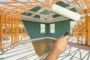 Man Using Paint Roller to Expose Finished Build of House Construction - Before and After. photo