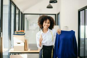 Calm curly brunette dark skinned woman on desk in office of fashion designer and holds tablet and smartphone. photo