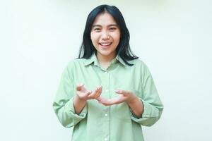 excited gorgeous asian woman wearing green over size clothes raising palms showing presenting gesture looking at camera with confident smile isolated on white background photo