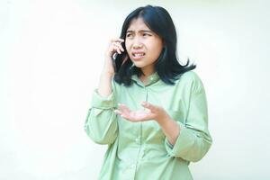 clueless asian woman wearing casual over sized green shirt raising palms showing i do not know gesture while speaking on smartphone isolated on white background, what do you want, looking away photo