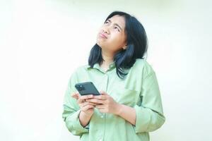 portrait of unhappy asian woman wearing over size green clothes looking above showing sad gloomy face expression confused using smartphone apps and online shopping isolated on white background photo