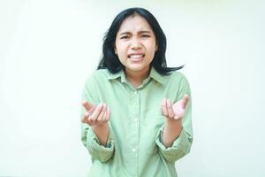 what do you want. angry asian woman wearing green casual clothes shrugging shoulders and raising palms forward show questioning gesture standing over isolated background, looking at camera photo