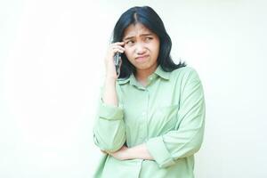 doubtful hesitant asian woman wearing casual over sized green shirt confused speaking on smartphone looking away showing pondering face expression with folding arms isolated on white background photo