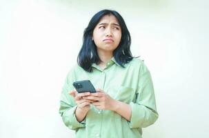 portrait of unhappy asian woman wearing over size green clothes look away showing sad gloomy face expression confused using smartphone apps and online shopping isolated on white background photo