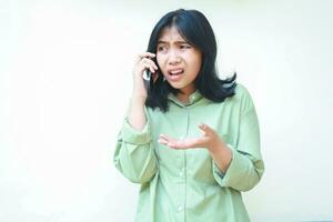 clueless asian woman wearing casual over sized green shirt raising palms showing i do not know gesture while speaking on smartphone isolated on white background, what do you want, looking away photo