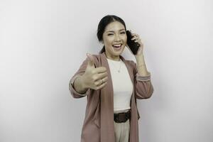 Excited young Asian woman employee is gesturing thumbs up for approval while holding a clipboard, isolated by white background photo