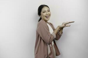 Excited Asian woman employee wearing cardigan pointing at the copy space beside her, isolated by white background photo