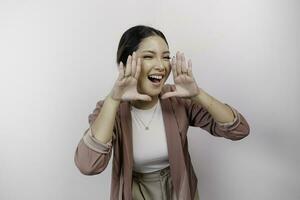 A young beautiful Asian woman employee wearing cardigan is shouting and screaming loud with a hand on her mouth, isolated by white background. photo