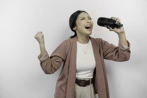Carefree Asian woman is having fun karaoke, singing in microphone while standing over white background photo