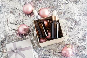 Two cosmetic bottles with a dropper with a natural facial skin care product lie in a festive New Year's box on a silver foil background. photo