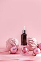 A cosmetic bottle with a dropper with facial skin care product stands on a transparent cube podium among New Year's pink balloons. Vertical view. photo