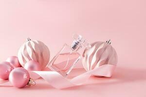 A chic bottle of women's perfume leans on a pink stylish ball in a New Year's composition with balloons and a ribbon. Front view. copy of space photo