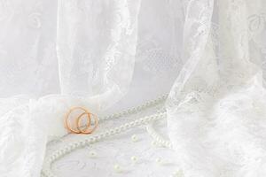 Delicate waves of a wedding veil or tulle with two wedding rings on it. wedding pearl beads of the bride. Front view. A copy of the space. photo