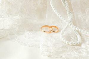 Delicate waves of a wedding veil or tulle with two wedding rings on it. wedding pearl beads of the bride. Front view. A copy of the space. photo