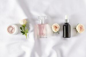un conjunto de productos cosméticos y perfumes para cuidado y belleza a hogar. botellas y Fresco flores plano disposición. parte superior vista. blanco satín antecedentes. foto