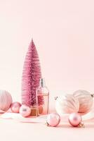 bottle of women's perfume or cosmetic spray on the background of a pink decorative Christmas tree and balloons. Vertical view. New Year's still life. photo