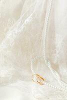 un elegante Boda antecedentes para diseño. antiguo tul con floral ornamento y un largo cuerda de perla rosario con dos oro anillos ensartado en a ellos. foto
