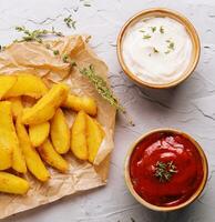 Baked fried potatoes with red and white sauces photo